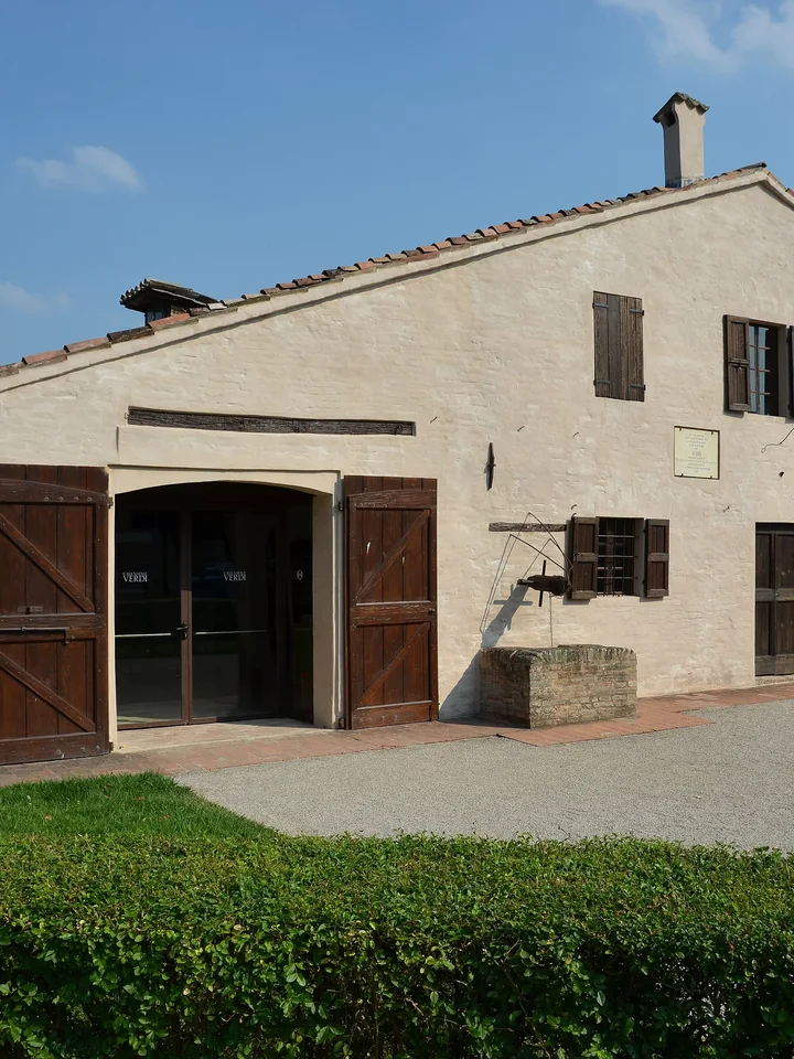 Das hell verputzte Landhaus, in dem Verdi geboren wurde, mit Fensterläden und einer Büste daneben