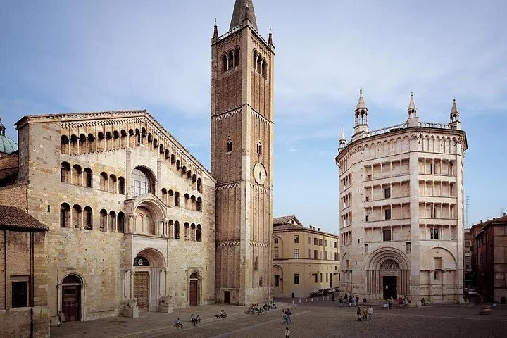Il duomo romanico di Parma con l'alto campanile in mattoni accanto al battistero ottagonale in marmo rosa sotto un cielo azzurro