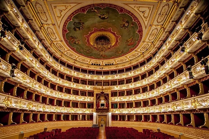 The horseshoe auditorium of the Teatro Regio di Parma with tiers of gilded boxes and a painted ceiling, all lit up