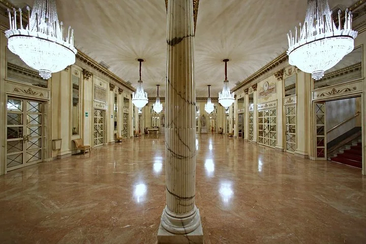 A marble hall with chandeliers, columns and mirrored doors in the La Scala museum in Milan