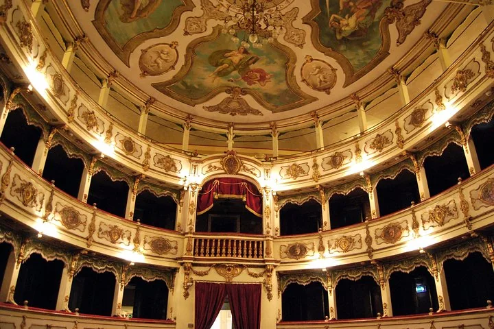 The auditorium of the Teatro Verdi in Busseto with tiers of cream and gold boxes, a central royal box with red curtains and a painted ceiling