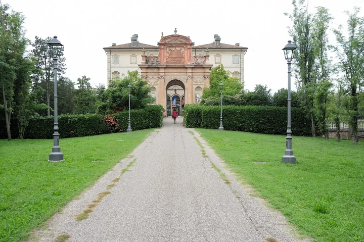 Eine lange Kiesallee zwischen Rasenflächen und Laternen, die zur Villa Pallavicino führt, einer hellen Villa mit barockem Portal